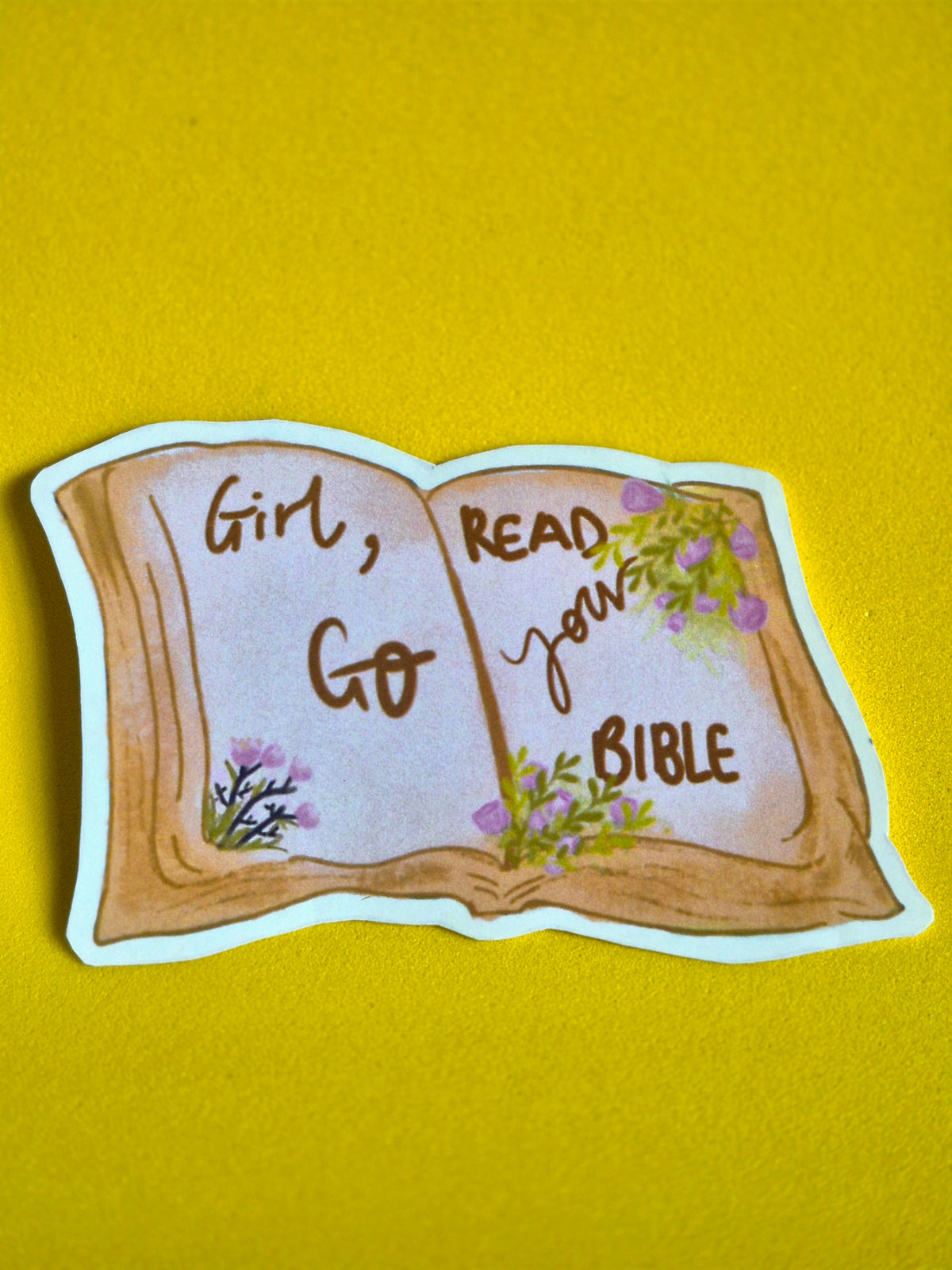 Sticker of an open book with text 'Girl, Go Read Your Bible' on a yellow background